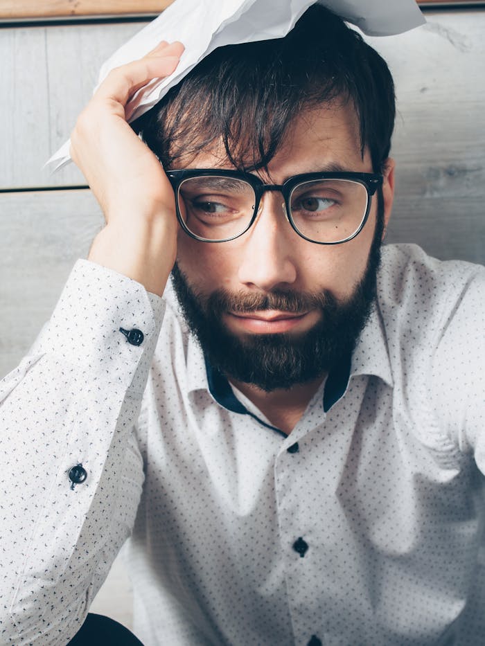 Portrait of a distressed man with glasses holding a paper, looking worried indoors.